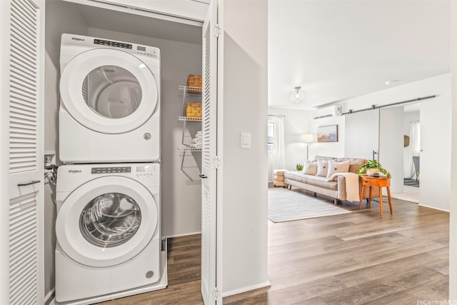 washroom featuring a wall mounted air conditioner, wood finished floors, laundry area, a barn door, and stacked washing maching and dryer