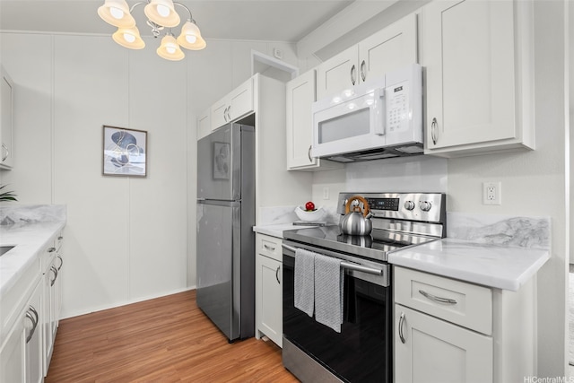 kitchen featuring light stone countertops, a notable chandelier, appliances with stainless steel finishes, light wood finished floors, and white cabinetry