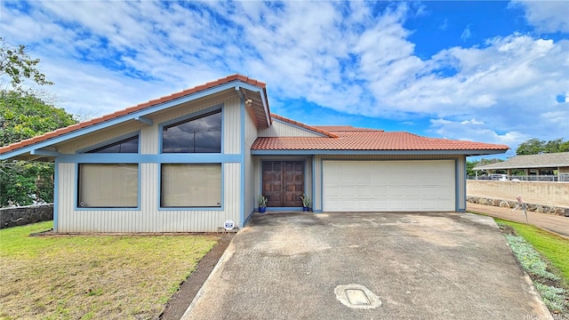view of front of house featuring a tiled roof, a garage, driveway, and a front yard