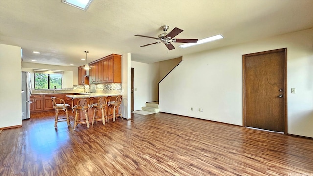 kitchen with freestanding refrigerator, a skylight, brown cabinets, dark wood-type flooring, and recessed lighting