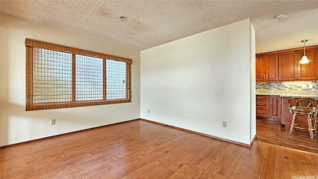 unfurnished living room with wood finished floors, a textured ceiling, and baseboards