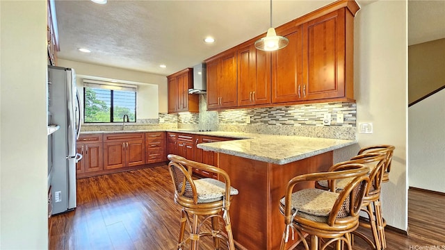 kitchen with freestanding refrigerator, a sink, a peninsula, dark wood-type flooring, and tasteful backsplash