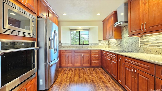 kitchen with appliances with stainless steel finishes, wall chimney range hood, a sink, dark wood finished floors, and decorative backsplash