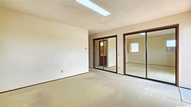 unfurnished bedroom featuring multiple closets, light carpet, a textured ceiling, and baseboards