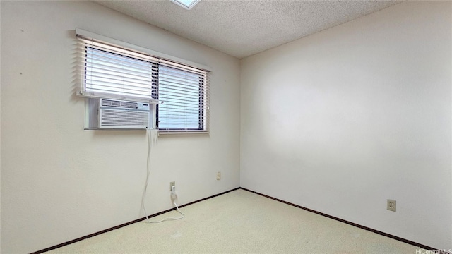 spare room featuring light carpet, a textured ceiling, cooling unit, and baseboards