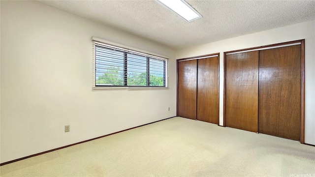 unfurnished bedroom with two closets, carpet floors, a textured ceiling, and baseboards
