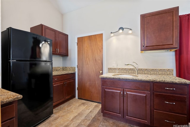 kitchen featuring light stone counters, freestanding refrigerator, and a sink