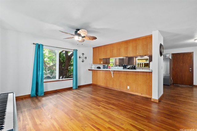 kitchen with light countertops, brown cabinetry, stainless steel fridge, and wood finished floors