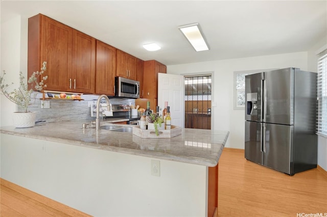 kitchen with a peninsula, brown cabinets, a sink, light wood finished floors, and stainless steel appliances