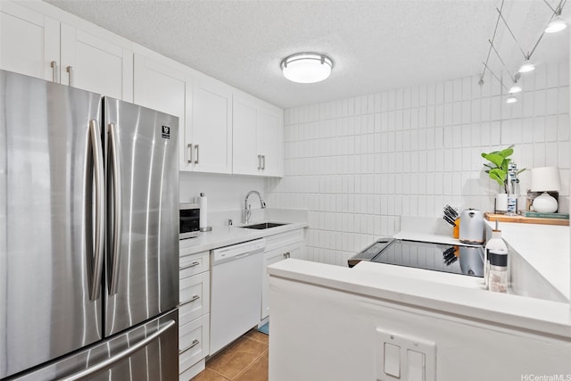 kitchen featuring freestanding refrigerator, a textured ceiling, dishwasher, a sink, and light countertops