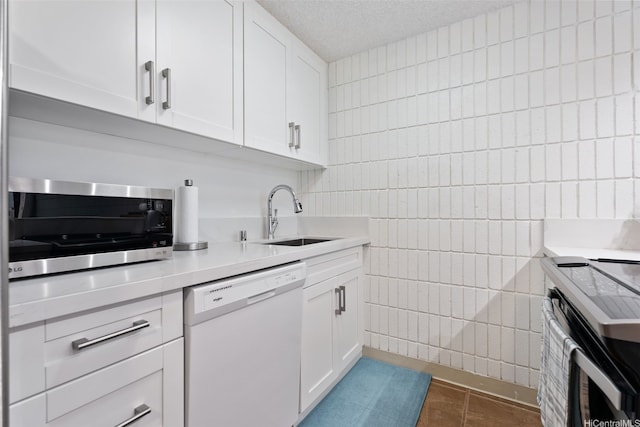 kitchen featuring tile walls, dishwasher, a sink, tile patterned floors, and light countertops