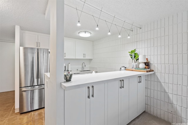 kitchen with a sink, tile walls, freestanding refrigerator, a textured ceiling, and white cabinets