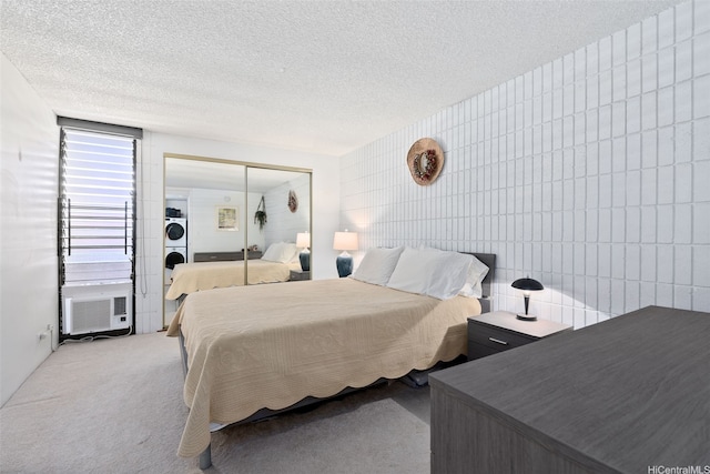 carpeted bedroom with tile walls, a closet, a textured ceiling, cooling unit, and stacked washer and dryer