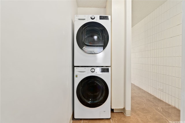washroom with laundry area, tile walls, stacked washer / drying machine, and light tile patterned floors