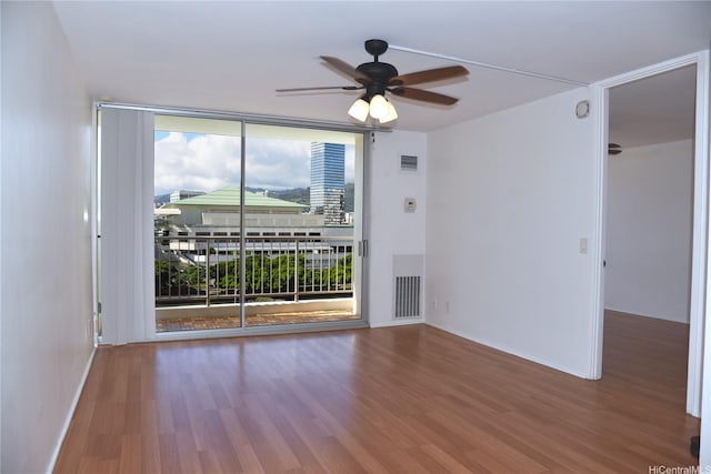 unfurnished room with expansive windows, a ceiling fan, visible vents, and wood finished floors