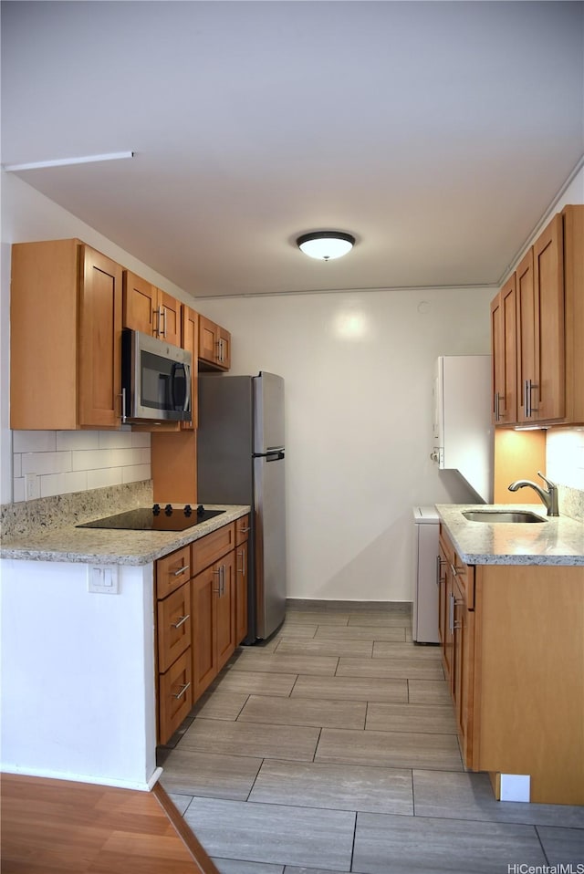 kitchen featuring wood tiled floor, decorative backsplash, appliances with stainless steel finishes, a sink, and light stone counters