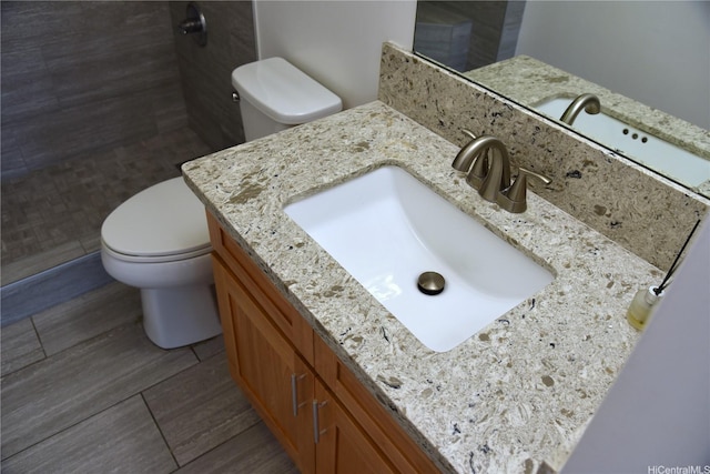 bathroom featuring vanity, a tile shower, toilet, and wood finished floors