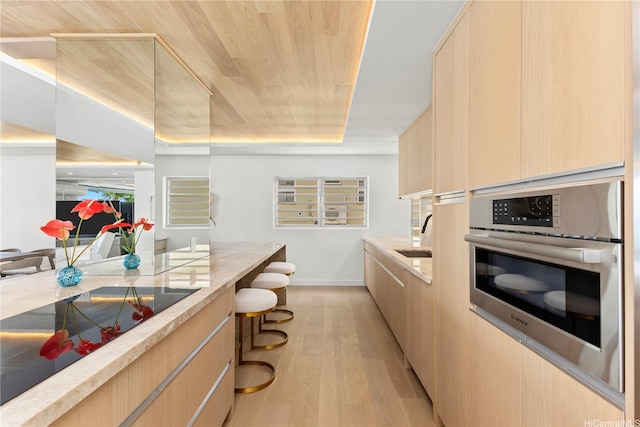 kitchen with oven, light stone countertops, light wood-style floors, light brown cabinets, and modern cabinets