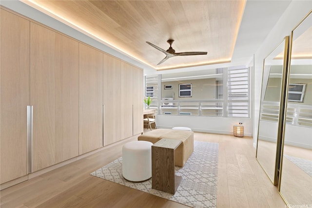 living area with a ceiling fan, light wood-style flooring, and a raised ceiling