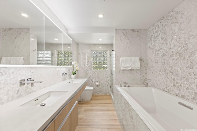 bathroom with double vanity, a garden tub, tile walls, a sink, and toilet