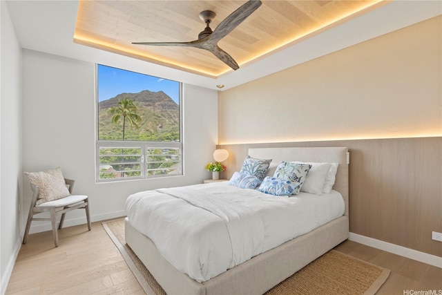 bedroom featuring baseboards, light wood finished floors, ceiling fan, and a tray ceiling