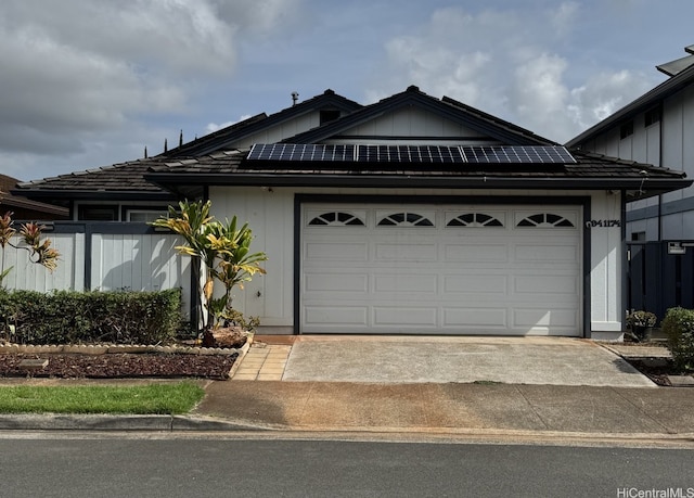 view of front of house with a garage, fence, concrete driveway, and solar panels