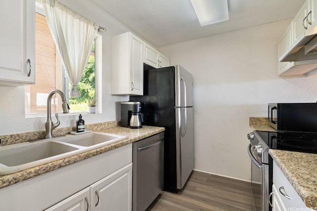 kitchen with wood finished floors, white cabinetry, under cabinet range hood, a sink, and stainless steel appliances