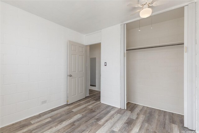 94-245 Leowahine St Unit 239, Waipahu, HI 96797 - unfurnished bedroom with concrete block wall, ceiling fan, wood finished floors, and a closet