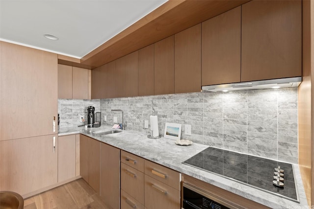 kitchen with a sink, light stone counters, under cabinet range hood, and black electric cooktop