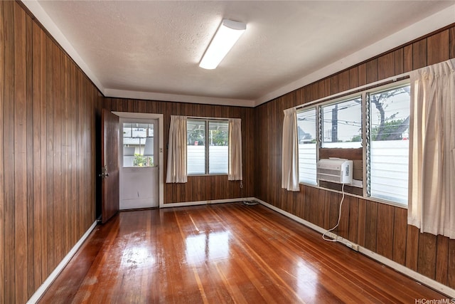 empty room with baseboards, a textured ceiling, wooden walls, and hardwood / wood-style flooring