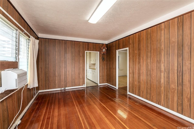 empty room featuring wood walls, hardwood / wood-style floors, baseboards, a textured ceiling, and cooling unit