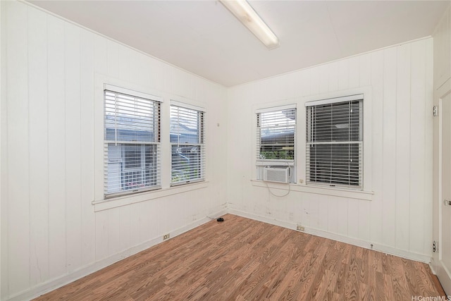 empty room featuring baseboards, wood walls, wood finished floors, and cooling unit