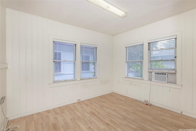 spare room featuring a healthy amount of sunlight, cooling unit, wooden walls, and wood finished floors