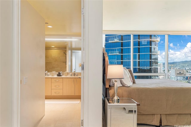 bedroom featuring connected bathroom, light flooring, a sink, and expansive windows