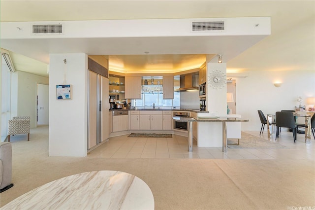 kitchen with light tile patterned floors, wall chimney range hood, a sink, a peninsula, and light carpet