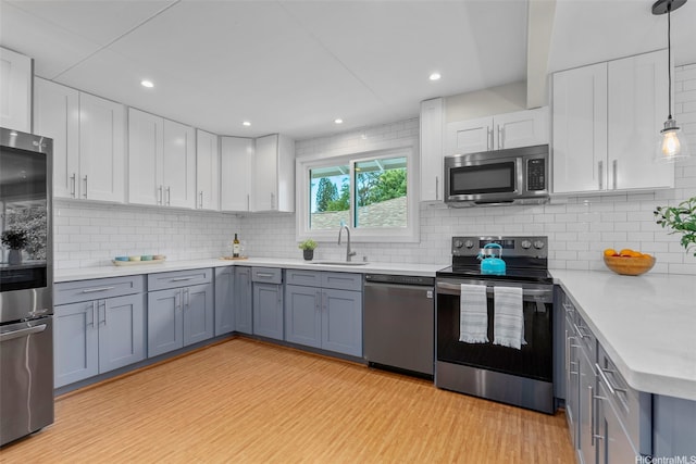 kitchen with stainless steel appliances, a sink, white cabinetry, light countertops, and light wood-type flooring