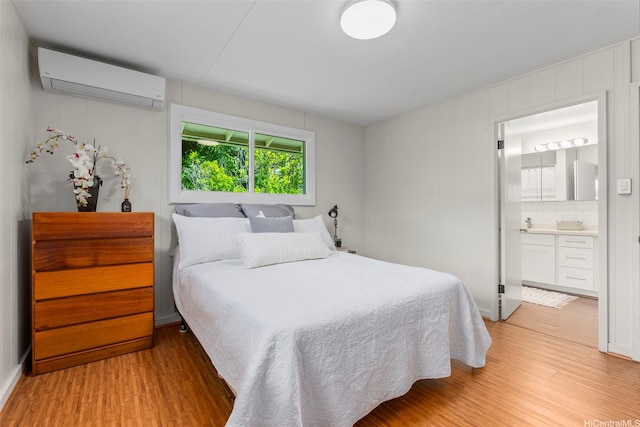 bedroom featuring an AC wall unit, light wood-type flooring, and ensuite bath