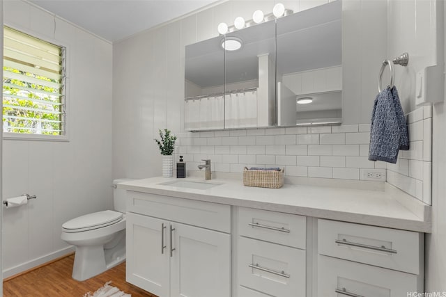 bathroom featuring toilet, wood finished floors, decorative backsplash, and vanity
