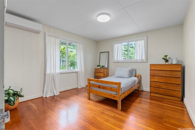bedroom featuring an AC wall unit, light wood-type flooring, multiple windows, and baseboards
