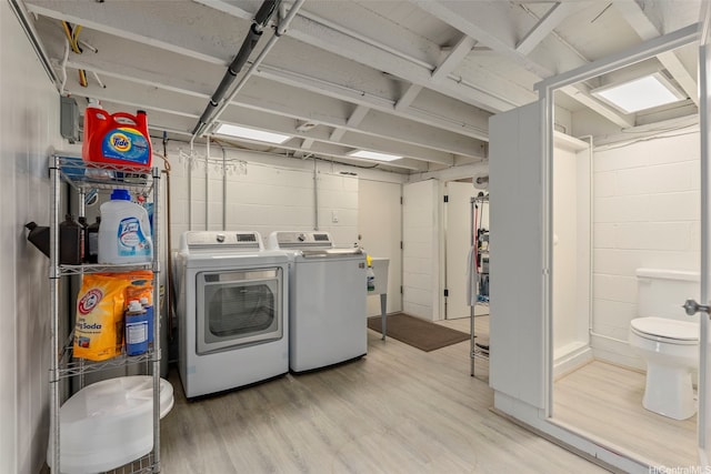 laundry room featuring separate washer and dryer, light wood-style flooring, and concrete block wall