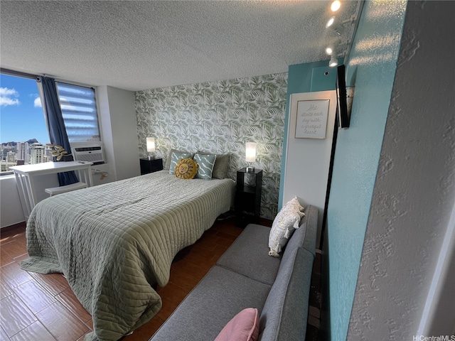 bedroom featuring a textured ceiling, cooling unit, an accent wall, and wallpapered walls