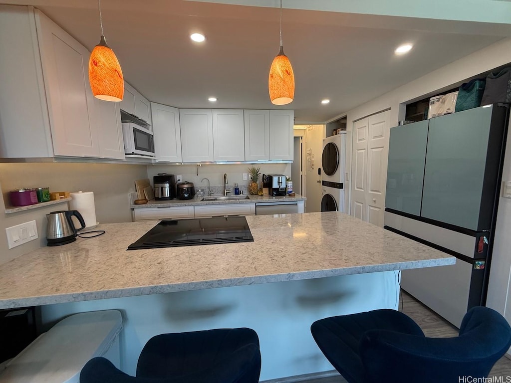 kitchen featuring a sink, stacked washing maching and dryer, stainless steel appliances, white cabinetry, and a peninsula