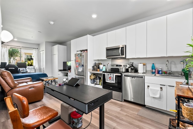 kitchen featuring stainless steel appliances, light wood finished floors, a sink, open floor plan, and light countertops