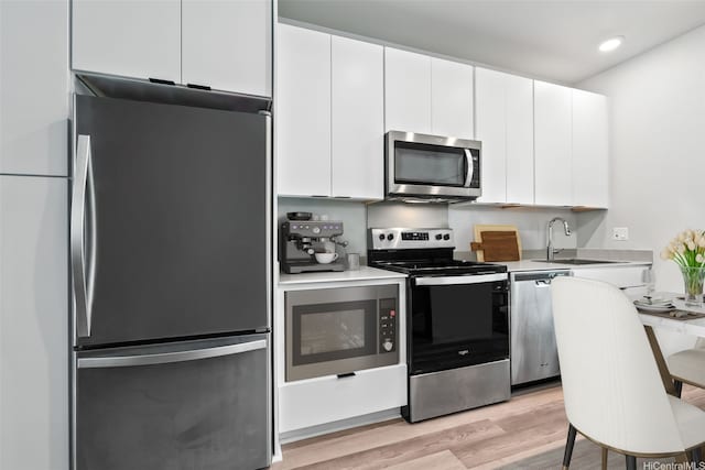 kitchen with a sink, stainless steel appliances, white cabinetry, and light wood-type flooring