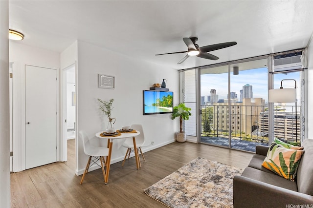 living area featuring ceiling fan, a wall mounted air conditioner, baseboards, wood finished floors, and expansive windows