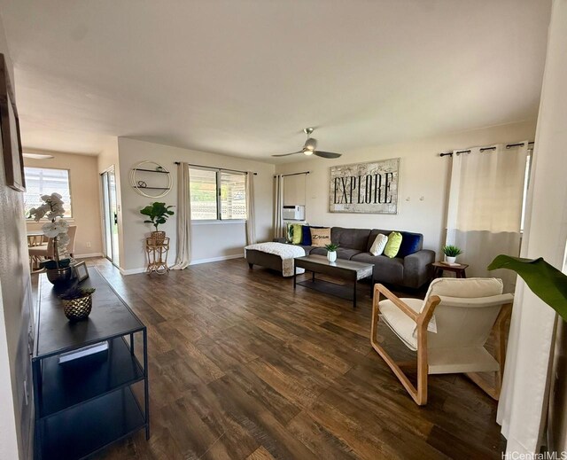 living room with dark wood-style flooring, a ceiling fan, plenty of natural light, and baseboards