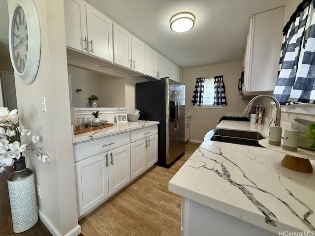 kitchen with a sink, light wood finished floors, white cabinetry, and stainless steel fridge with ice dispenser