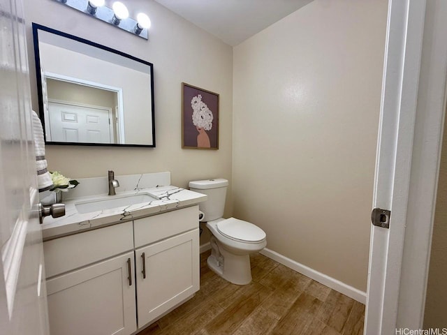 half bathroom with baseboards, vanity, toilet, and wood finished floors