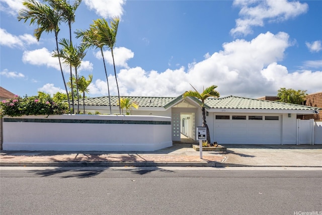 view of front facade featuring fence, driveway, a garage, stucco siding, and a tiled roof