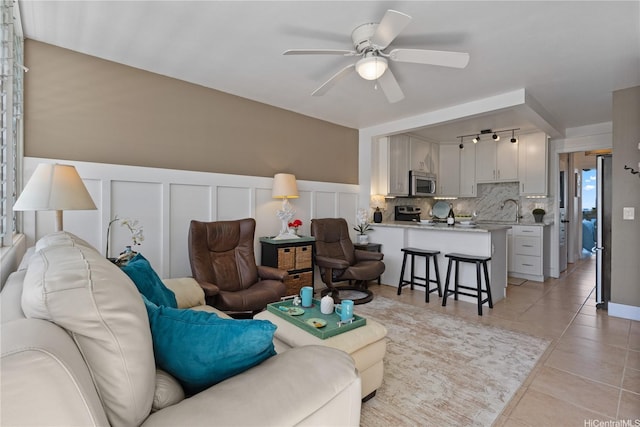 living room featuring light tile patterned flooring, wainscoting, a decorative wall, and a ceiling fan